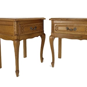 Puede incluir: Dos mesitas de noche de madera con un cajón cada una. Las mesitas de noche tienen un acabado marrón claro y tallas ornamentadas. Los cajones tienen tiradores de metal simples.