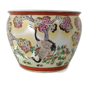 May include: A white ceramic planter with a yellow background and a floral design featuring pink and white flowers, green leaves, and two cranes. The planter has a red rim.