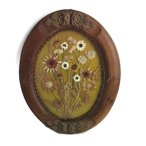 May include: Oval wooden frame with a pressed flower design. The frame is dark brown with carved details and a yellow background. The flowers are a variety of colors, including white, yellow, orange, and red.