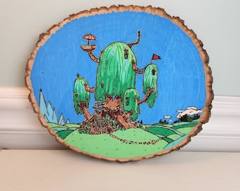 May include: A hand-painted wooden slice featuring a whimsical treehouse with multiple levels and a blue sky background. The treehouse is surrounded by green foliage and has a red flag on top.