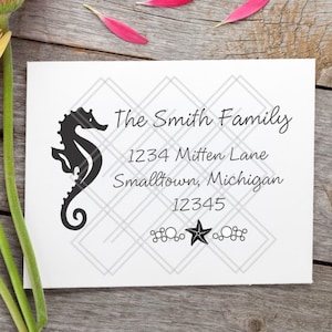 May include: A white card with a seahorse graphic and the text "The Smith Family" with an address and zip code. The card is decorated with a gray diamond pattern and a black star. Three colorful gerbera daisies and pink petals are on a wooden surface.