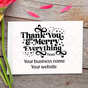 May include: A greeting card with the message "Thank You & Merry Everything" and business details, accompanied by vibrant gerbera daisies in red, yellow, and orange. The card is on a wooden surface.