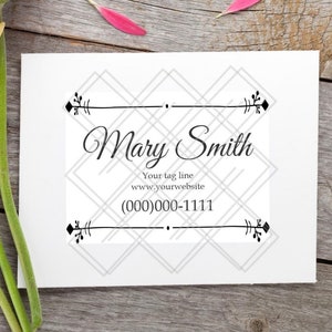 May include: A white business card with the name "Mary Smith" in elegant script, framed by a geometric design. The card also includes a tagline, website, and phone number. Bright orange, yellow, and pink gerbera daisies rest on a wooden surface.