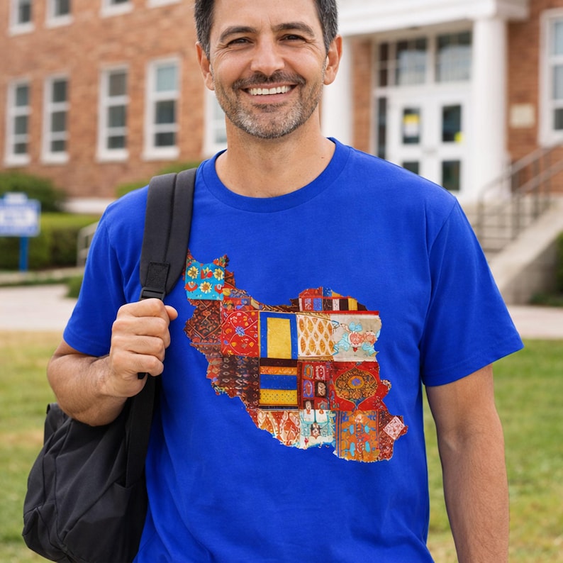 May include: A royal blue t-shirt featuring a colorful patchwork design in the shape of a country. The design incorporates various patterns and colors, including red, yellow, blue, and orange. The shirt is short-sleeved and worn by a person with a black backpack.