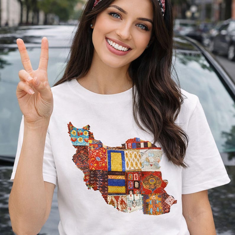 May include: White t-shirt featuring a colorful, patchwork design in the shape of a country. The design incorporates various patterns and colors, including red, blue, yellow, and gold. The shirt is short-sleeved.