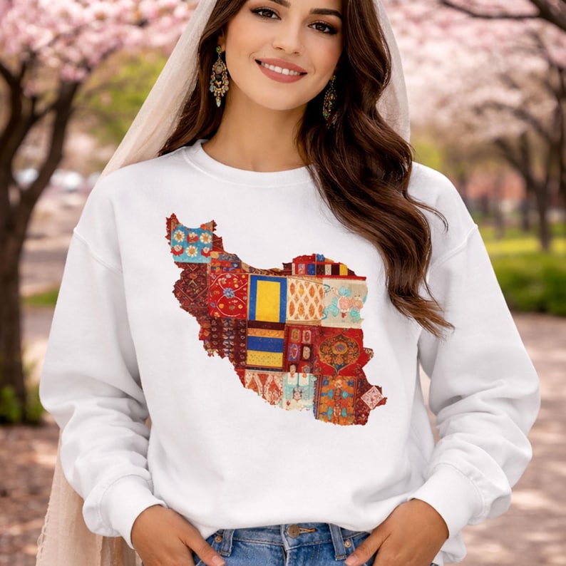 May include: White sweatshirt featuring a colorful patchwork design in the shape of Iran. The design incorporates various patterns and colors, including red, blue, yellow, and orange. The sweatshirt is a casual style.