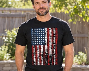 Puede incluir: Una camiseta negra de manga corta con un gráfico rectangular de la bandera estadounidense en el pecho. El diseño de la bandera tiene una textura desgastada y envejecida con estrellas blancas sobre fondo azul y rayas rojas y blancas.