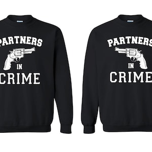 May include: Two black sweatshirts with white text that reads "Partners in Crime" and a graphic of a revolver.