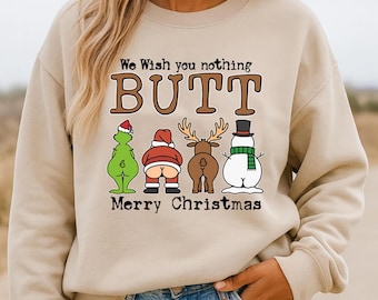 May include: A beige crewneck sweatshirt featuring a graphic print with the text "We Wish you nothing BUTT Merry Christmas" and illustrations of the backsides of a green creature, Santa Claus, a reindeer, and a snowman wearing a top hat and scarf.