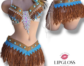 May include: A two-piece costume featuring a tan bra top and skirt adorned with brown fringe, light blue lace trim, turquoise studs, and clear rhinestones. The bra includes a central rhinestone applique and shoulder feathers. The skirt has side lacing.