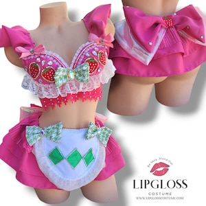 Peut inclure: Ensemble de lingerie rose et blanc sur le thème de la fraise et du nœud. Le soutien-gorge est orné d'une dentelle et la jupe a un tablier blanc avec des accents de diamants verts. La jupe a également un grand nœud rose à l'arrière.