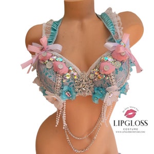 May include: A teal and white lace bra with pink and white bows, seashells, and rhinestones. The bra has a halter style strap and a silver chain attached to the bottom.