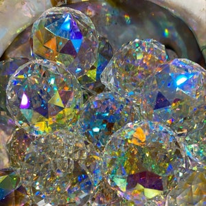 May include: A group of iridescent crystal ball ornaments with a rainbow prism effect. The crystals are faceted and reflect light in a variety of colours.