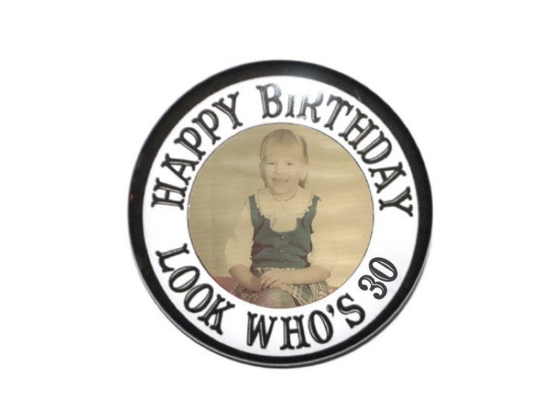 May include: A black and white round button with the text "Happy Birthday Look Who's 30" in a circle around a photo of a young girl.