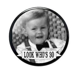 May include: A black and white circular button with a vintage photo of a young child wearing a bow tie and suspenders. The text "LOOK WHO'S 30" is displayed on a banner below the photo.