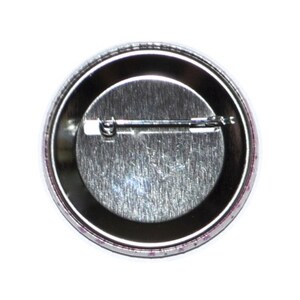 Op de afbeelding: De achterkant van een ronde knop met een zilveren metalen achterkant en een pin aan de achterkant.