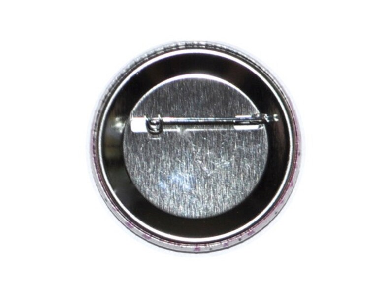 Op de afbeelding: De achterkant van een ronde knop met een zilveren metalen achterkant en een pin aan de achterkant.