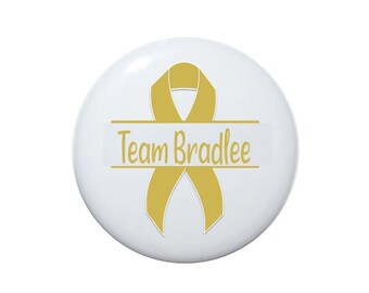 May include: A white button with a gold ribbon and the text "Team Bradlee" printed on it.