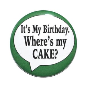 May include: A green and white button with the text "It's My Birthday. Where's my CAKE?" in a speech bubble.