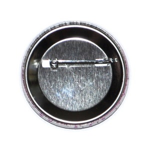 May include: The back of a round button with a silver metal backing and a pin on the back.