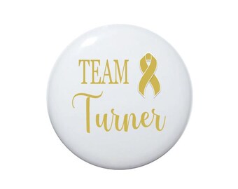 May include: White button with gold text that reads "TEAM Turner" and a gold ribbon.