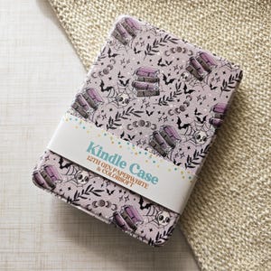 Puede incluir: Una funda Kindle de color lila claro con un patrón repetido de libros, murciélagos, telarañas, calaveras y lunas. La funda tiene una banda blanca con el texto "Kindle Case 12th Gen Paperwhite & Colorsoft".
