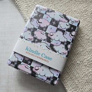 May include: Kindle case with a whimsical design featuring pastel clouds, bats, and stars on a black and white checkered background. The case has a white band with the text "Kindle Case 11th Gen Paperwhite".