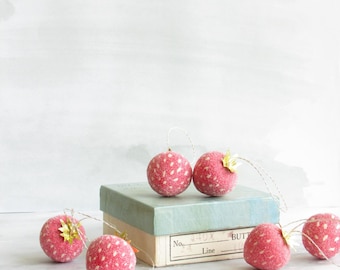 May include: Pink, strawberry-shaped decorations with white speckles and gold leaf detailing. Each ornament has a string for hanging. The decorations are displayed on a vintage blue-green box.