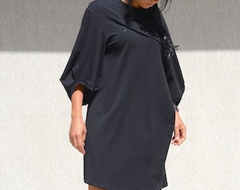 Pode incluir: Um vestido preto solto, de comprimento até ao joelho, com uma bainha ligeiramente assimétrica. O vestido tem um estilo simples e casual e é usado com sandálias de plataforma pretas.