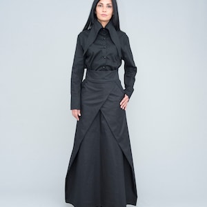 Può includere: Un completo nero composto da una camicia a maniche lunghe con colletto alto e una gonna a portafoglio. La gonna ha un design unico con pannelli sovrapposti, creando un effetto a strati. L'outfit è realizzato in tessuto nero tinta unita.