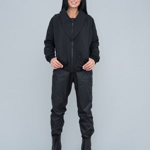May include: A black zip-up jacket with a wide collar and matching black trousers. The model is wearing black ankle boots.