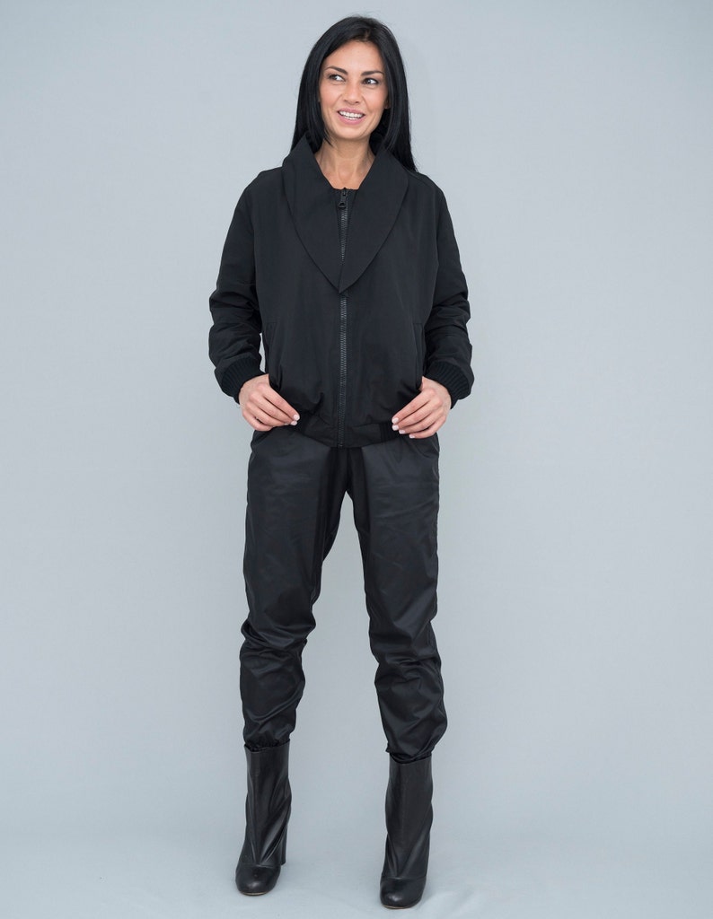 May include: A black zip-up jacket with a wide collar and matching black trousers. The model is wearing black ankle boots.