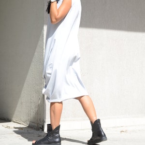 May include: A woman wearing a light gray hooded dress with a sleeveless design. She is wearing black ankle boots with a strap across the ankle.