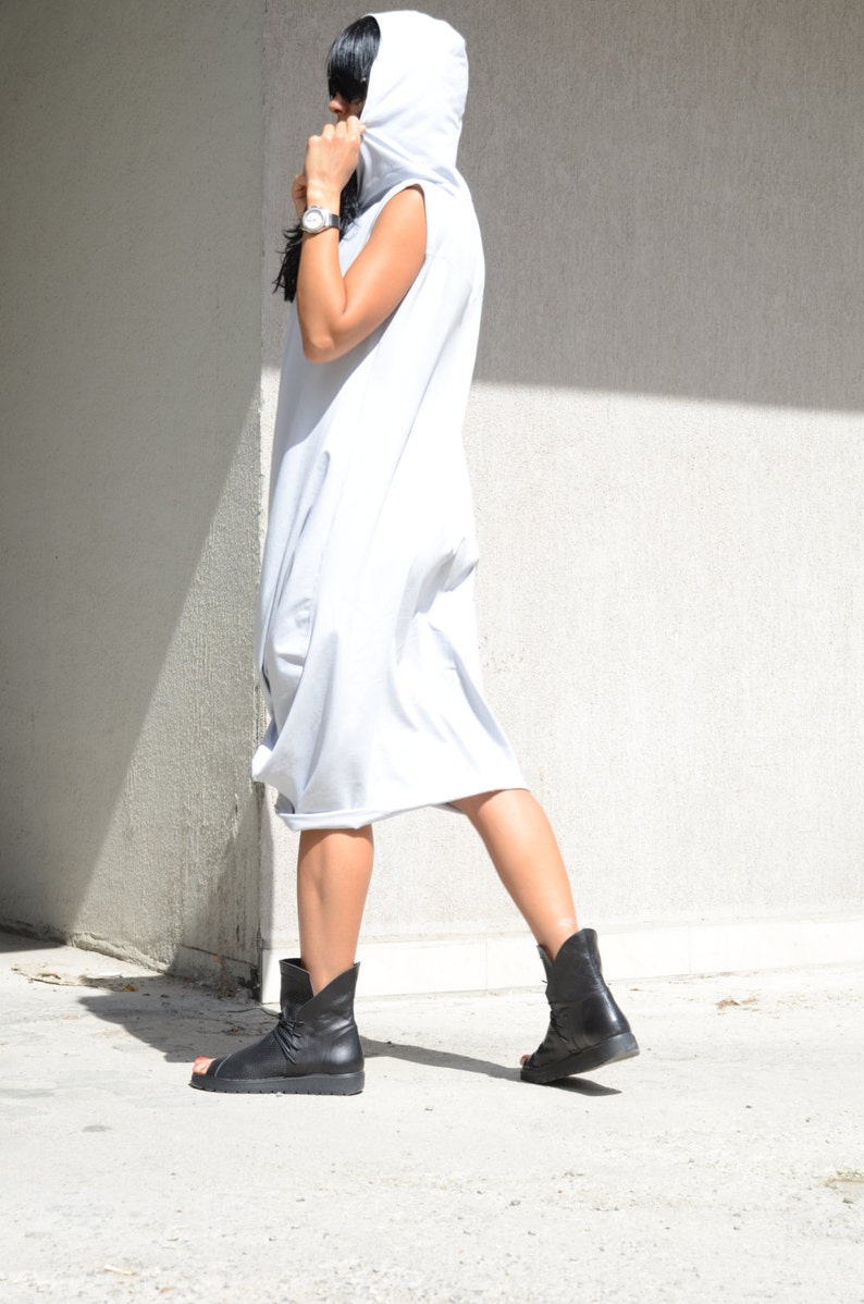 May include: A woman wearing a light gray hooded dress with a sleeveless design. She is wearing black ankle boots with a strap across the ankle.