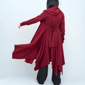 May include: A long, burgundy hooded cardigan with a tie at the waist. The cardigan has a flowing, asymmetrical hemline.