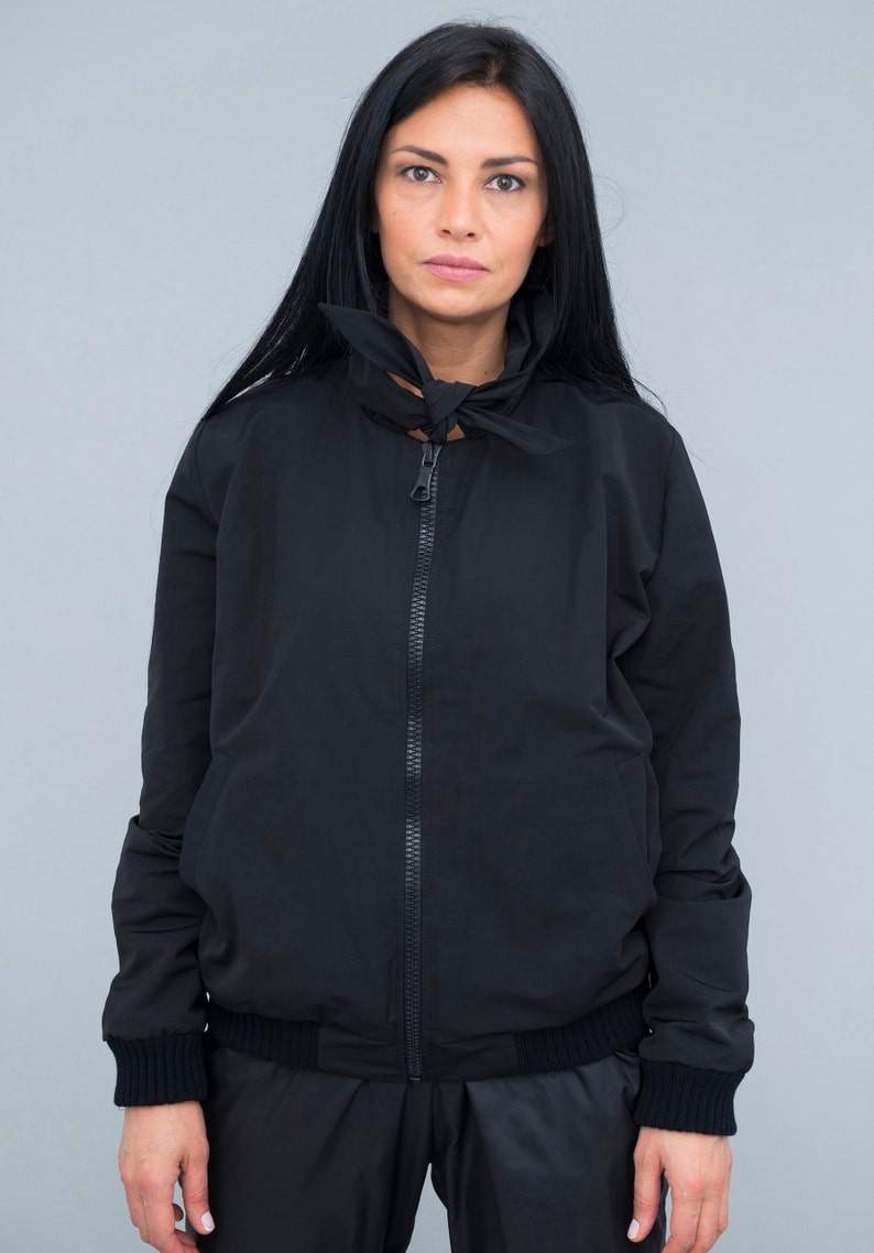 May include: A black zip-up jacket with a high collar and a tied bow detail at the neck.