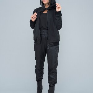 May include: A black bomber jacket with a black zipper and a black turtleneck top. The model is wearing black trousers and black ankle boots.