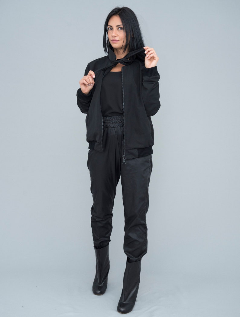 May include: A black bomber jacket with a black zipper and a black turtleneck top. The model is wearing black trousers and black ankle boots.