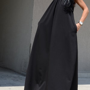 Pu&ograve; includere: Un abito maxi nero con scollo halter e una silhouette ampia e fluida.