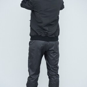 May include: A black hooded jacket with a zip fastening and a black elastic waistband. The jacket is worn over black trousers with a similar elastic waistband.