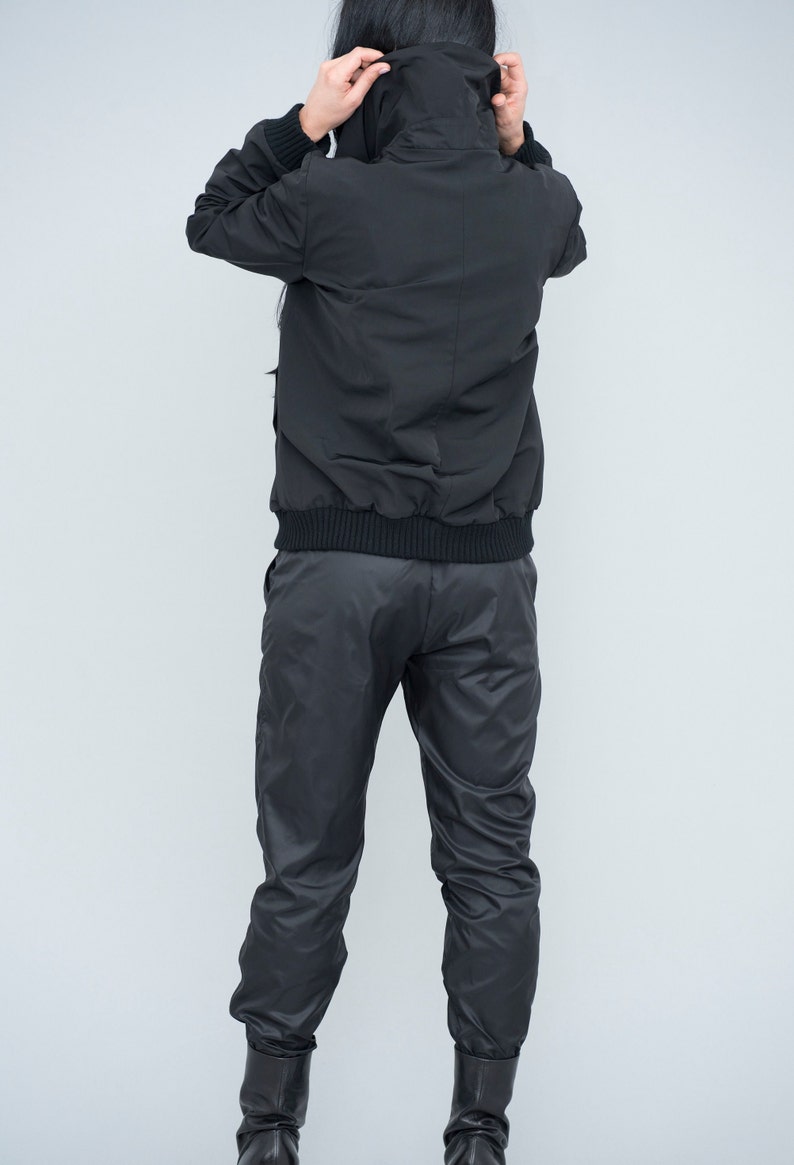 May include: A black hooded jacket with a zip fastening and a black elastic waistband. The jacket is worn over black trousers with a similar elastic waistband.