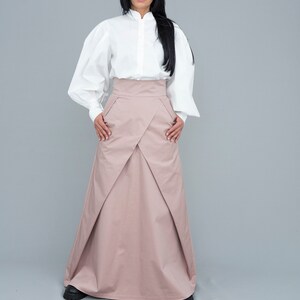 May include: A long, blush-colored skirt with a high waist and a pleated design. The skirt is made of a lightweight fabric and has a flowing silhouette.
