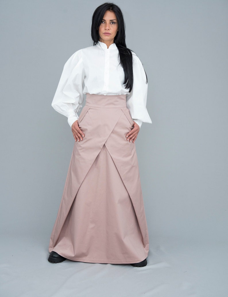 May include: A long, blush-colored skirt with a high waist and a pleated design. The skirt is made of a lightweight fabric and has a flowing silhouette.