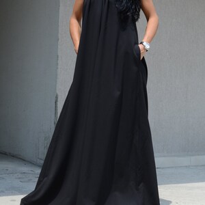 Pu&ograve; includere: Un abito maxi nero con scollo halter e un dettaglio drappeggiato sul d&eacute;collet&eacute;. L'abito ha tasche sui lati e una silhouette fluida.