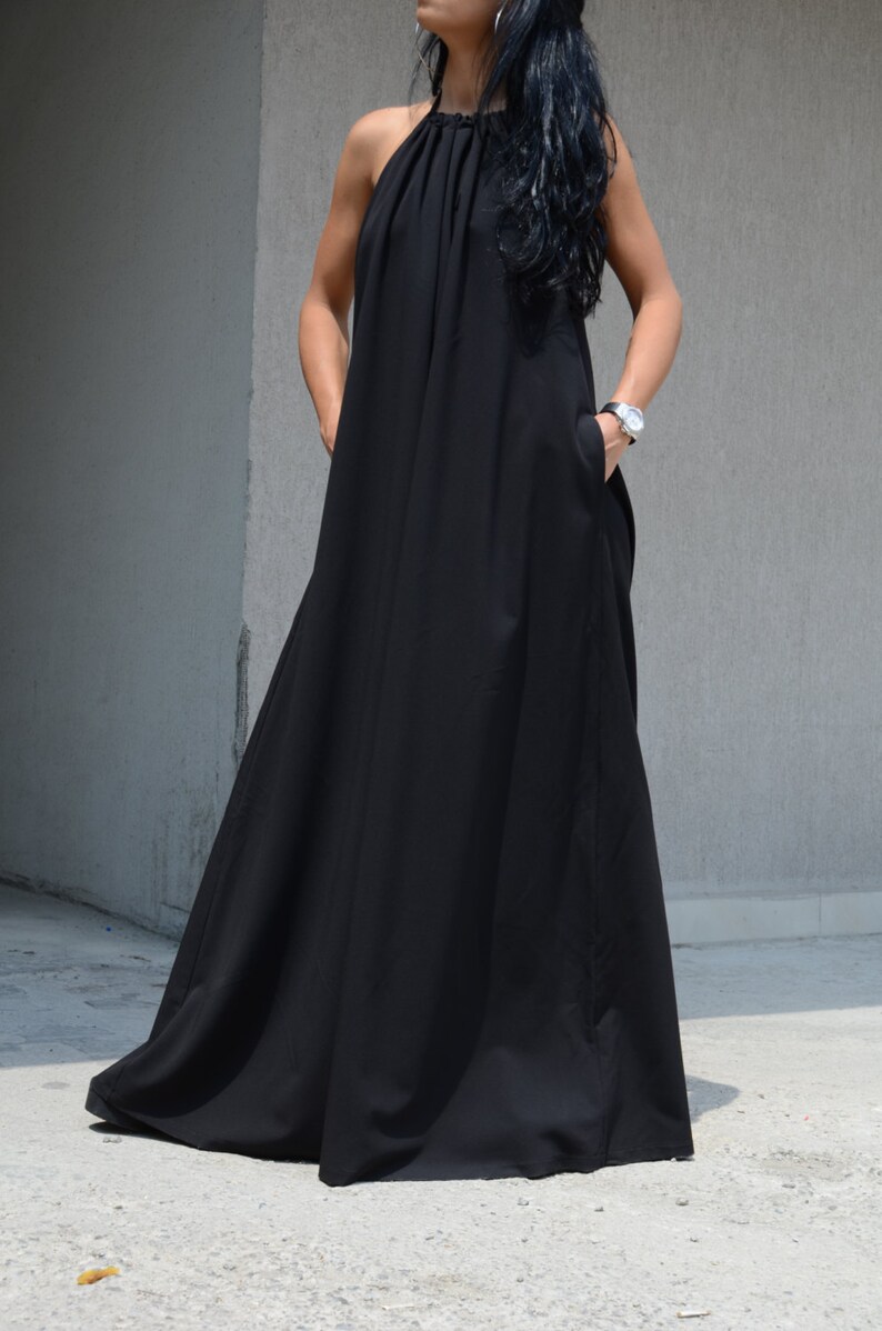 Pu&ograve; includere: Un abito maxi nero con scollo halter e un dettaglio drappeggiato sul d&eacute;collet&eacute;. L'abito ha tasche sui lati e una silhouette fluida.