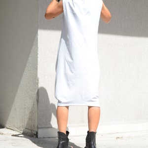 May include: A white sleeveless hooded dress with a long, flowing silhouette. The dress is made of a soft, comfortable fabric and has a relaxed fit. The model is wearing black ankle boots.