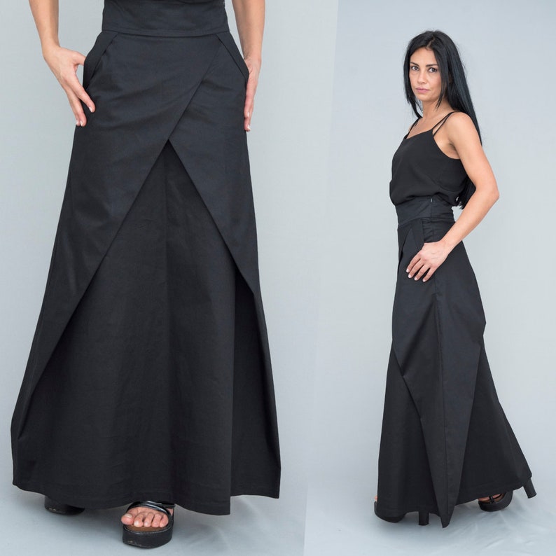 May include: A black maxi skirt with a unique asymmetrical design. The skirt has a high waist and a flowing silhouette.