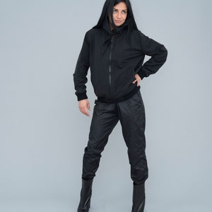 May include: A black hooded jacket with a zip fastening and a matching pair of black trousers. The model is wearing black boots.