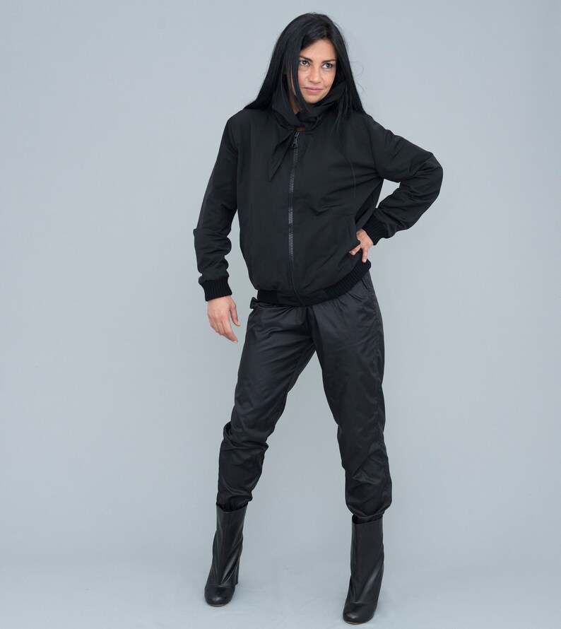 May include: A black hooded jacket with a zip fastening and a matching pair of black trousers. The model is wearing black boots.