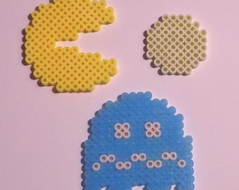 Peut inclure: Trois personnages en pixel art : un Pac-Man jaune, un fantôme vert clair et un fantôme bleu avec des yeux blancs. Les personnages sont faits de petites perles rondes, couramment utilisées dans les projets de bricolage.